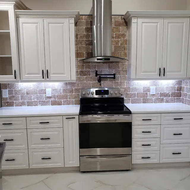 Stainless range and chimney hood framed by white shaker cabinets and brick backsplash
