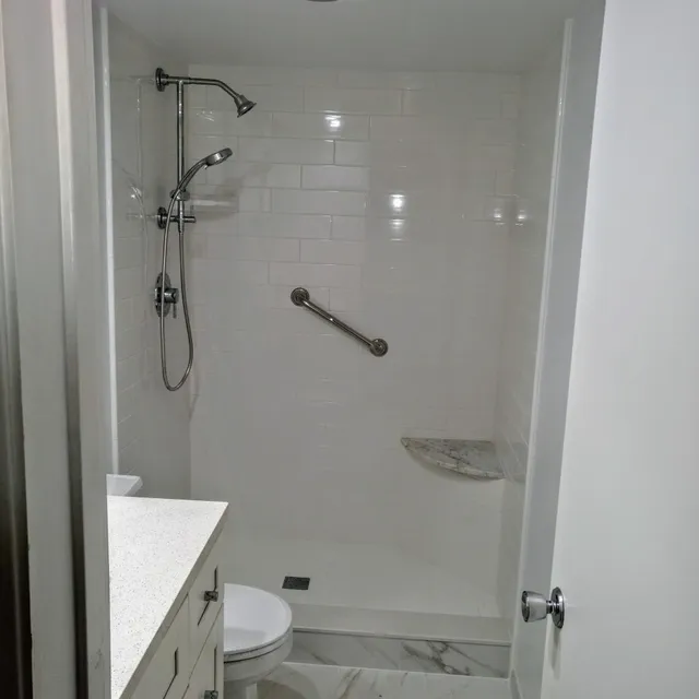 White tile shower with handheld shower head and grab bar