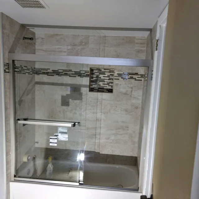 Tiled shower with sliding glass enclosure and mosaic accent