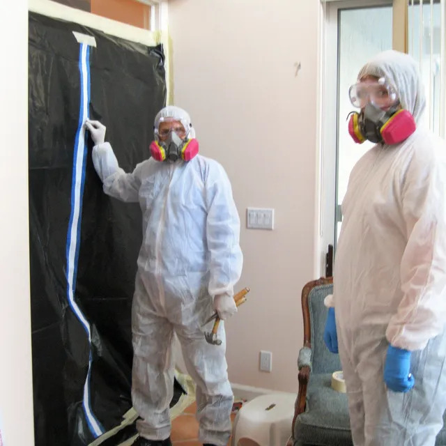 Technicians in protective suits behind a containment wall